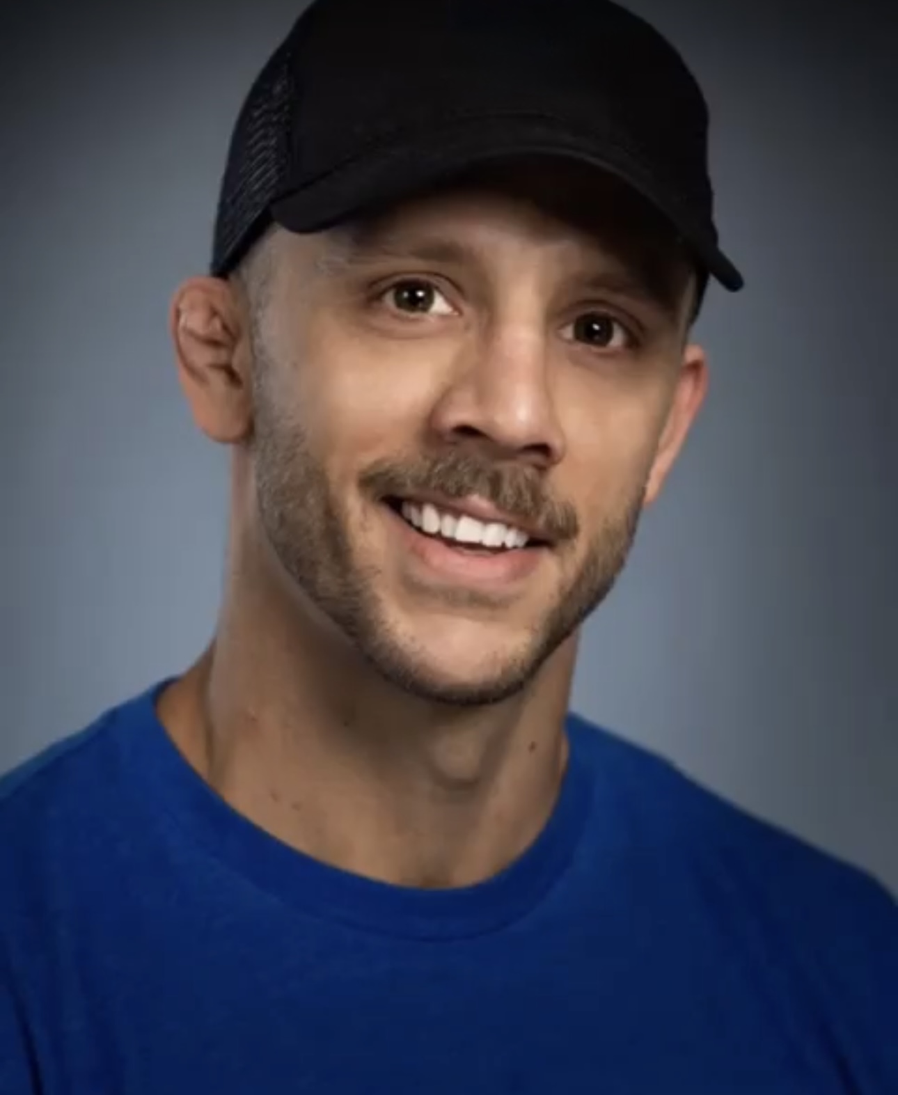 Man in blue shirt wearing a black ball cap smiling for a picture